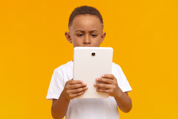 Isolated image of serious concentrated African little boy holding generic touchpad tablet using...