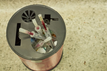Used needles and cap, broken glass of used drug in container of biohazard disposal