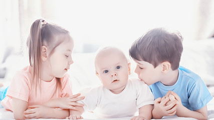 Children lie on the bed next to the newborn baby, little sister.