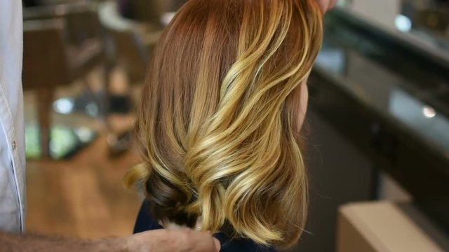 Hairdresser making red hair looks perfect in his hands