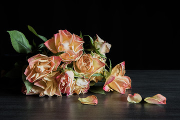 A bouquet of withered roses lies on a table against a black background. Concept death and sadness.