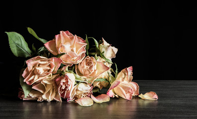 A bouquet of withered roses lies on a table against a black background. Concept death and sadness.