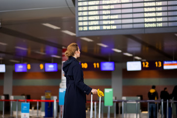 Stewardess with luggage looks at Informational display in airport terminal