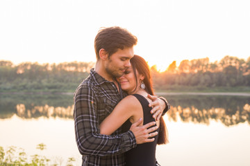 Romantic and people concept - young couple hugging together near the river or lake and enjoying summer time