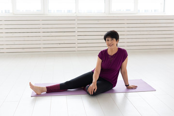 People, sport, yoga and healthcare concept - Smiling middle-aged woman sitting on exercise mat