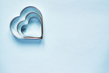 Three metal cookie cutters in heart shape on light blue background with copy space