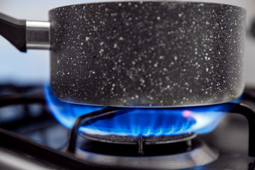 Gas stove with an open blue flame, cook on it dish in ladle