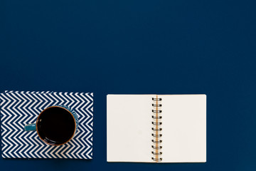 top view of cup of black coffe and clean notebook on blue background with copy space.
