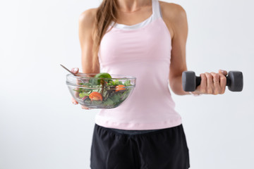 Sport, healthy lifestyle, people concept - close up of young woman with salad and a dumbbell. She is smiling and enjoying the healthy lifestyle