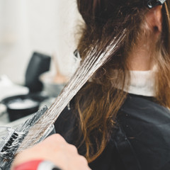 Young professional hairdresser applying dye on clients hair