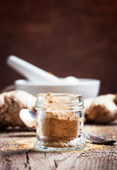 Ground ginger in glass jar and fresh ginger root, vintage wooden kitchen table background, selective focus