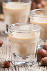 Liquor with nuts in small shot glass on the old wooden table background, selective focus
