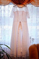 White wedding dress for the bride hanging on the window