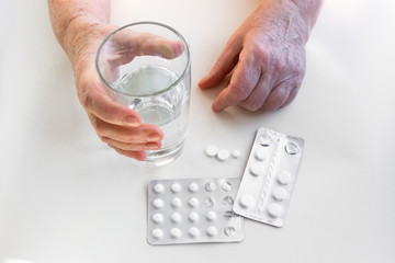 Hands of an elderly person with pills, packaging of medication. Glass of water. The concept of maintaining life in old age, treatment and health.