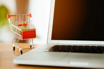 shopping concept - Empty Shopping Cart, laptop, on rustic wooden background.