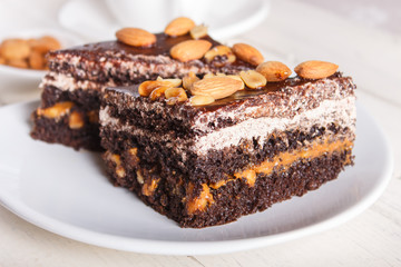 Chocolate cake with caramel, peanuts and almonds on a white wooden background.