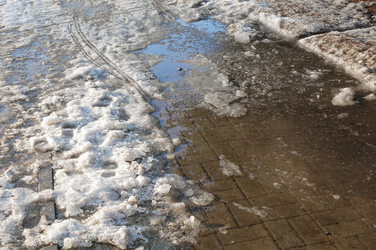 Closeup photograph of melting snow on a pavement made of gray concrete tiles.