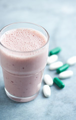 Glass of Protein Shake with milk and raspberries. BCAA amino acids and L - Carnitine capsules in background. Sport nutrition. Bright tone background. Close up. Copy space. 