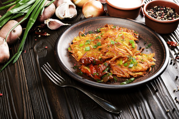Homemade tasty potato pancakes in clay dish with sun-dried tomatoes and sour cream