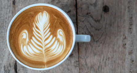 Close up caffe latte art coffee with flat milk in white ceramic coffee cup on wooden table in coffee shop cafe restaurant with morning sunlight. Concept for coffee lover or relaxation mood.