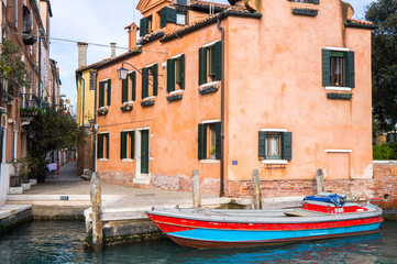 Fototapeta na wymiar Red blue boat in Venice staying in still canal water parked near orange house 