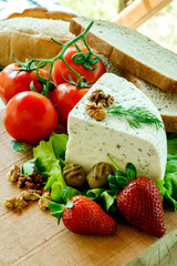 white cream cheese with herbs and spices on a fresh leaf of lettuce, wooden Board decorated with ripe strawberries, walnuts, delicious tomatoes and olives roasted on the grill