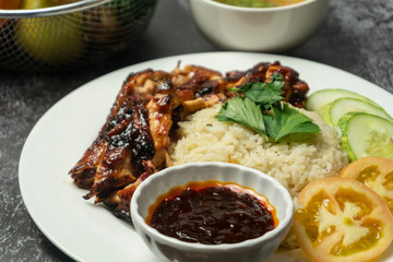 a plate of chicken rice with soup and sauce isolated on dark background.