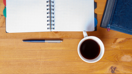 office desk with notebook and blue pen and cup of coffee with copy space. Top view