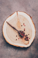Peppercorns in a wooden spoon on a stump. Top view, flat lay.