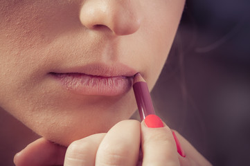 Close up of hands applying lipstick on female facial skin