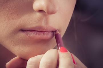 Naklejka premium Close up of hands applying lipstick on female facial skin