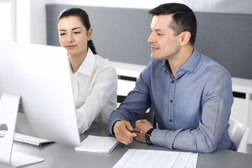 Cheerful smiling businessman and woman working with computer in modern office. Headshot at meeting or workplace. Teamwork, partnership and business concept 
