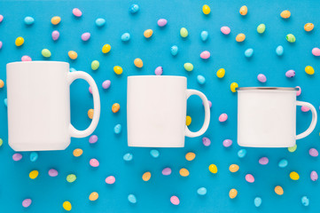 Three white mugs 15oz, 11oz and 10oz, mockup for Easter on a bright blue background with candy...