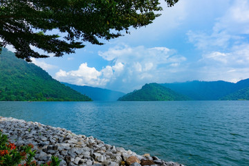 Natural landscape of mountain and lake in blue sky day with green leaves in foreground at top left corner