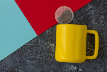 Yellow mug on black stone background. Teabag, red and blue paper. With copy space.