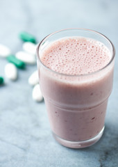Glass of Protein Shake with milk and raspberries. BCAA amino acids and L - Carnitine capsules in background. Sport nutrition. Bright tone background. Close up. Copy space. 