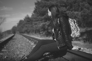 Pensive woman sitting on railway. Side view in black and white of young thoughtful woman sitting on rail and looking away in nature