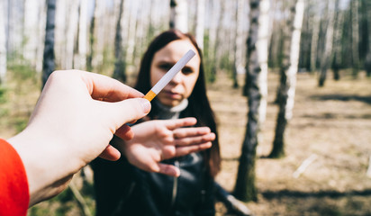 Woman refusing to take cigarette. Crop male hand offering cigarette to woman meeting stop gesture...