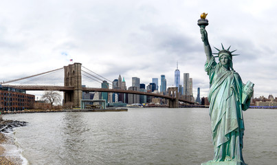 Panorama view of The Statue of Liberty with Brooklyn Bridge and Manhattan downtown sky scraper with cloud blue sky background, Financial district lower Manhattan, New York City, USA.