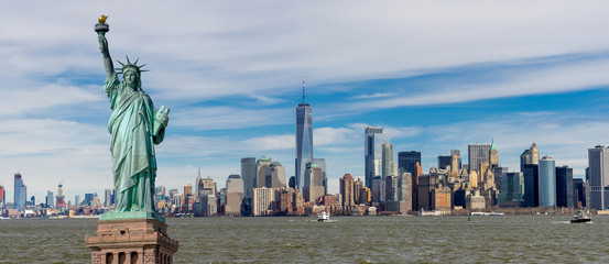 Panorama view of The Statue of Liberty with One World Trade Center and Manhattan downtown sky scraper with cloud blue sky background, Financial district lower Manhattan, New York City, USA.