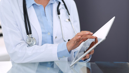 Female doctor hands using digital tablet  while sitting at glass desk at hospital office. Medicine and healthcare concept