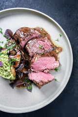 Barbecue aged sliced venison sirloin with mushroom in gammon red wine sauce and mashed potatoes with ramson as top view a modern design plate