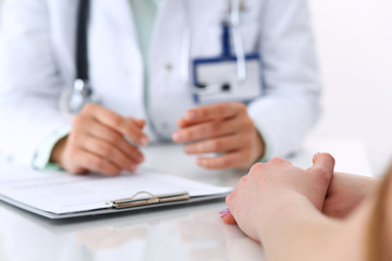 Unknown doctor and patient talking while sitting at the desk in hospital office, close-up of human hands. Medicine and health care concept