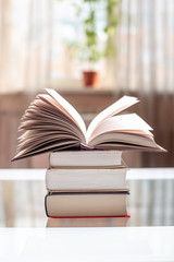 Open book on a stack of books on a table in a bright room. Education and reading of paper books