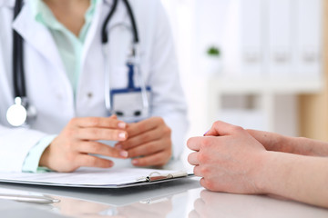 Fototapeta premium Unknown doctor and patient talking while sitting at the desk in hospital office, close-up of human hands. Medicine and health care concept