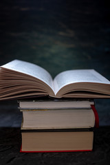 Open book on a stack of books on a table on a dark background. Exam preparation in schools and colleges