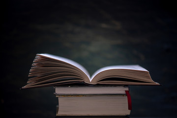 Open book on a stack of books on a table on a dark background. Exam preparation in schools and colleges