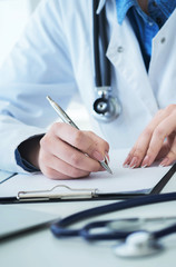 Female doctor filling up prescription form or patient history list at clipboard pad during physical exam or disease prevention while sitting at the desk in hospital closeup. - 258763775