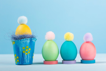 Dyed bright Easter eggs in the nest and in stands with colorful pompons on a blue background.
