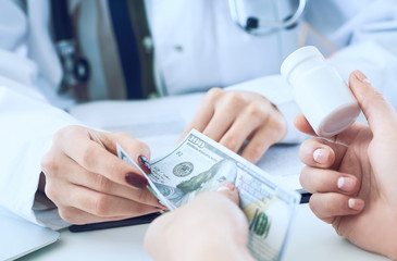 Female doctor hands gives jar of pills to patient hand and receives money in return closeup.